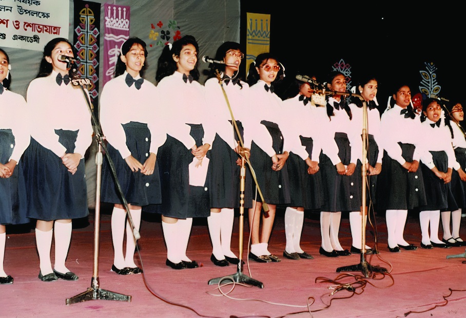 A children’s choir in matching uniform singing on a stage. A children’s choir performing in Kochi Kontho uniform.