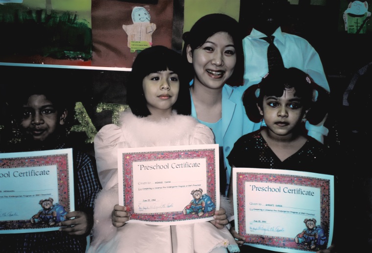 Three children holding preschool certificates beside a smiling teacher